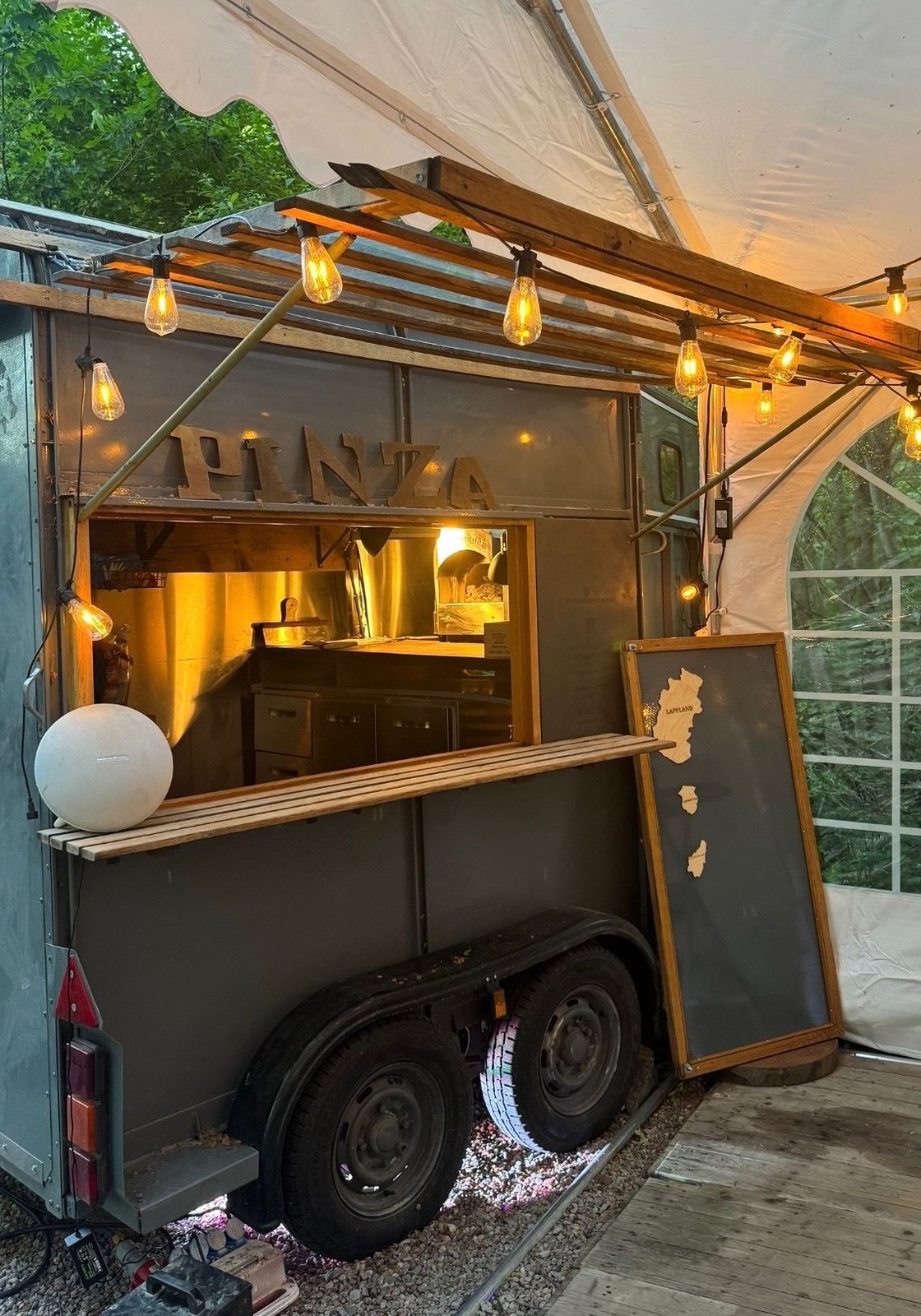 Pizzatrucken med skylten Pinza i ett partytält, lamporna tända och luckan öppen