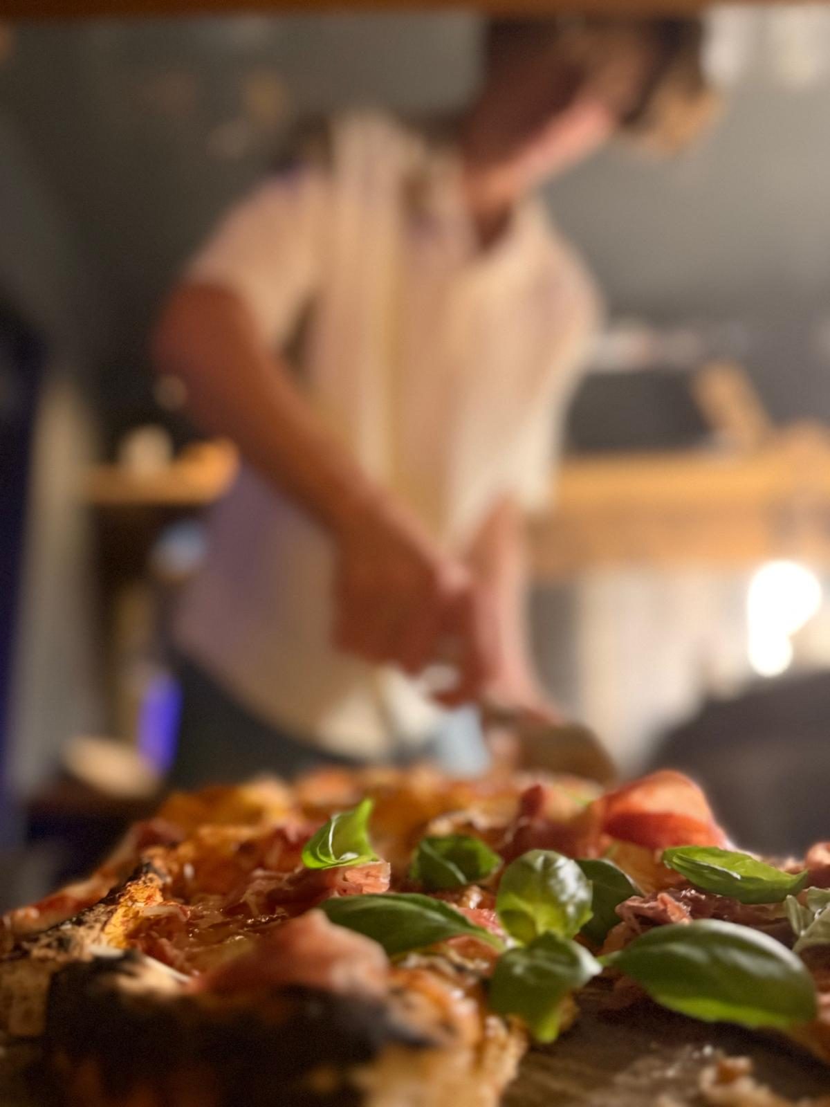Nygräddad pizza med skinka och basilika, bagaren i bakgrunden