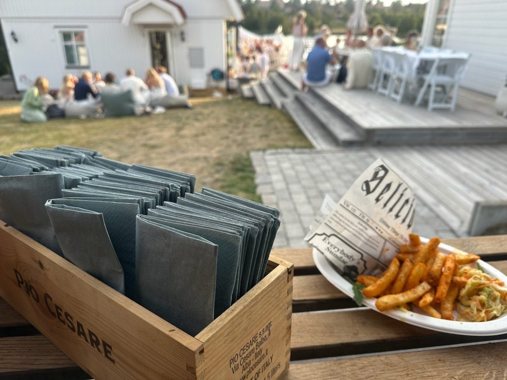 Servetter och en tallrik vid luckan, gästerna sitter i trädgården i bakgrunden